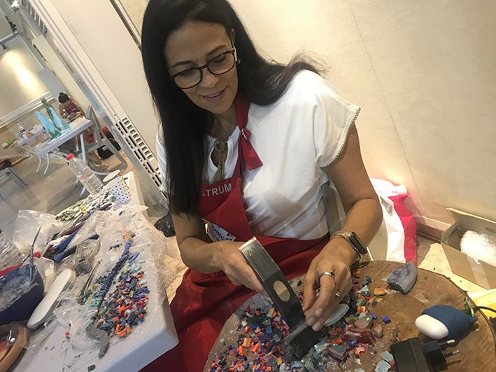 Ronit Strum cutting glass tesserae with a mosaic hammer at her worktable