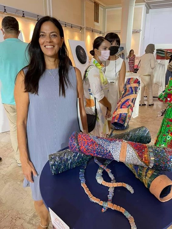Ronit Strum standing beside one of her mosaic sculptures at an exhibition