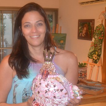 Ronit Strum smiling, holding one of her mosaic sculptures